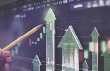 main tenant un crayon devant un visuel boursier (© Shutterstock)